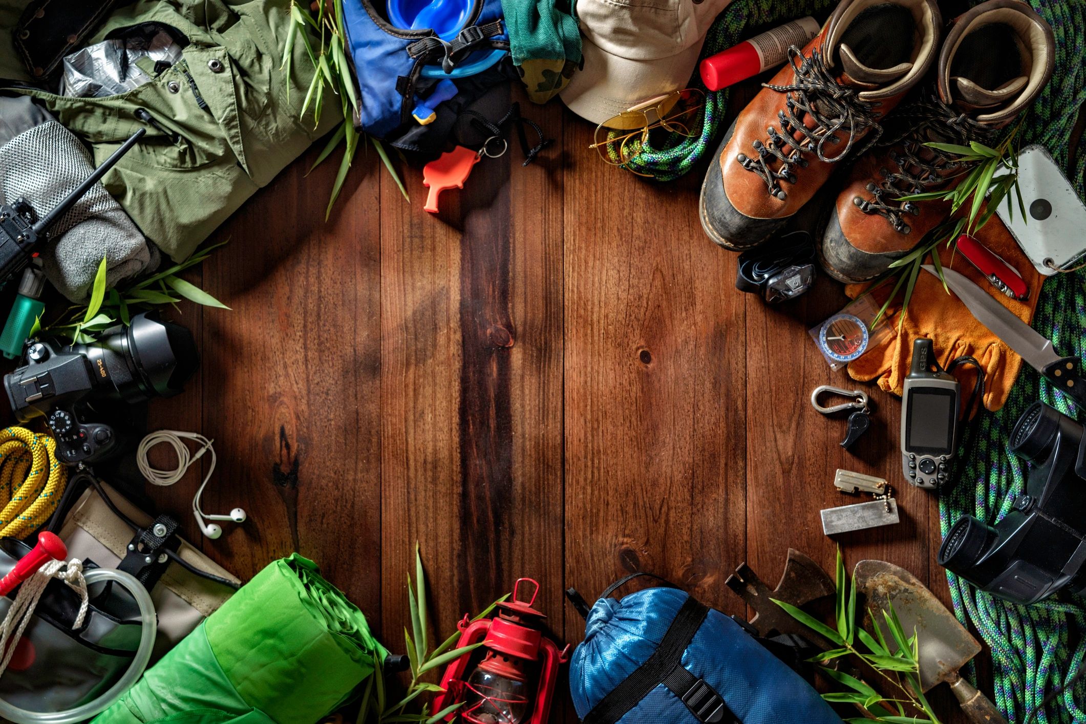 Outdoor gear and safety equipment arranged on wooden surface, including hiking boots, ropes, a camera, a compass, gloves, and various tools, emphasizing preparation for mountain climbing and hiking adventures.