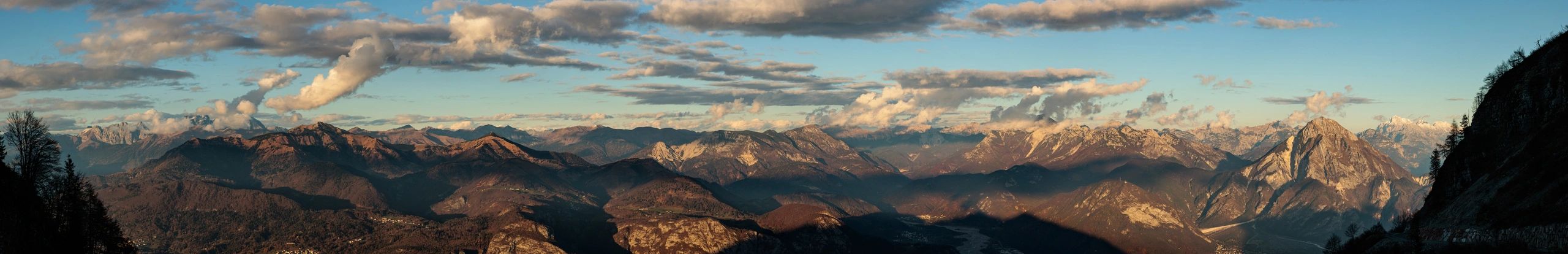Panoramic view of mountainous terrain under a partly cloudy sky, showcasing diverse peaks and valleys, reflecting the landscapes encountered in mountaineering adventures.