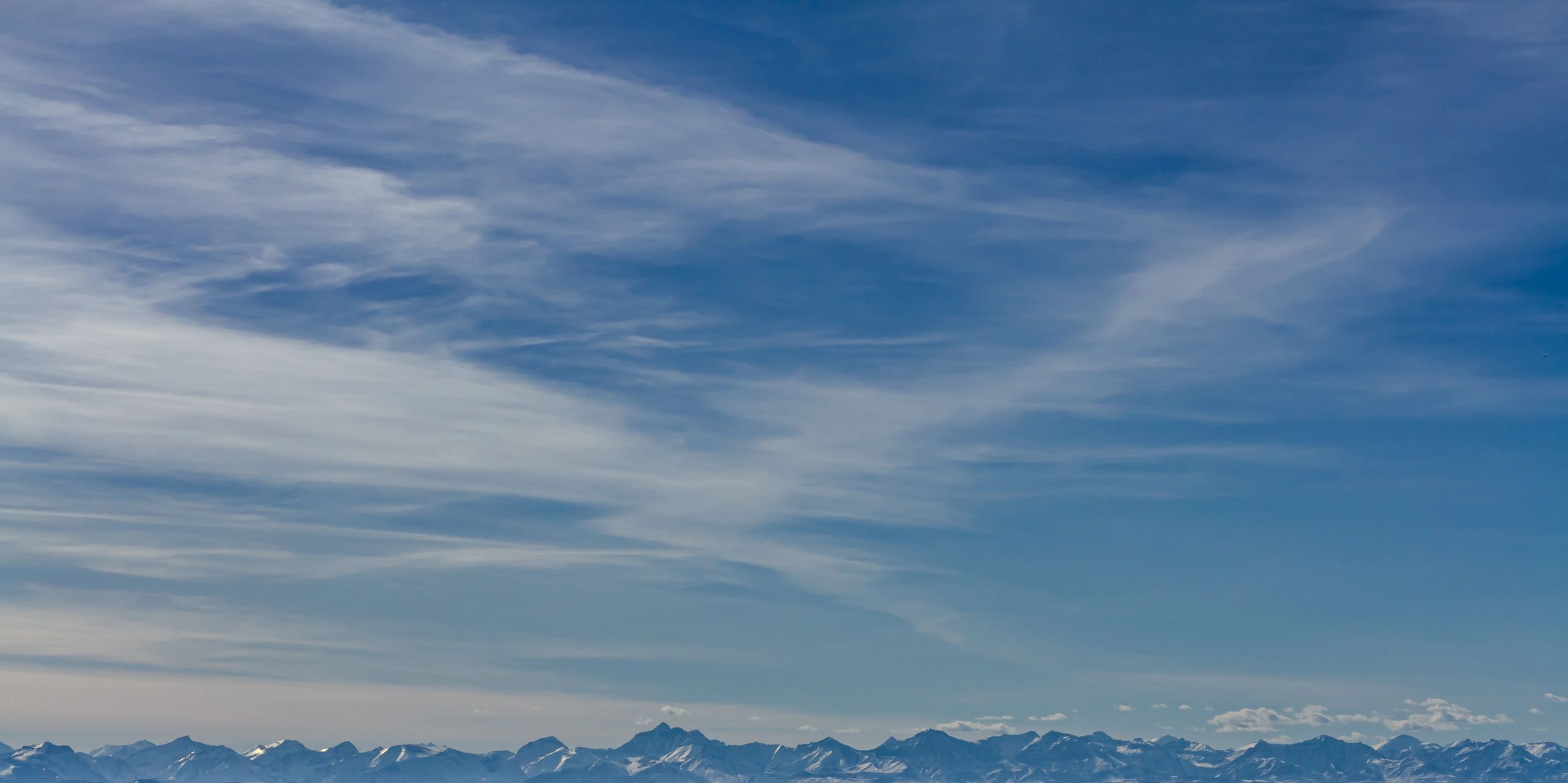 Scenic mountain landscape under a clear blue sky with wispy clouds, illustrating the terrain and conditions for hikers and climbers.