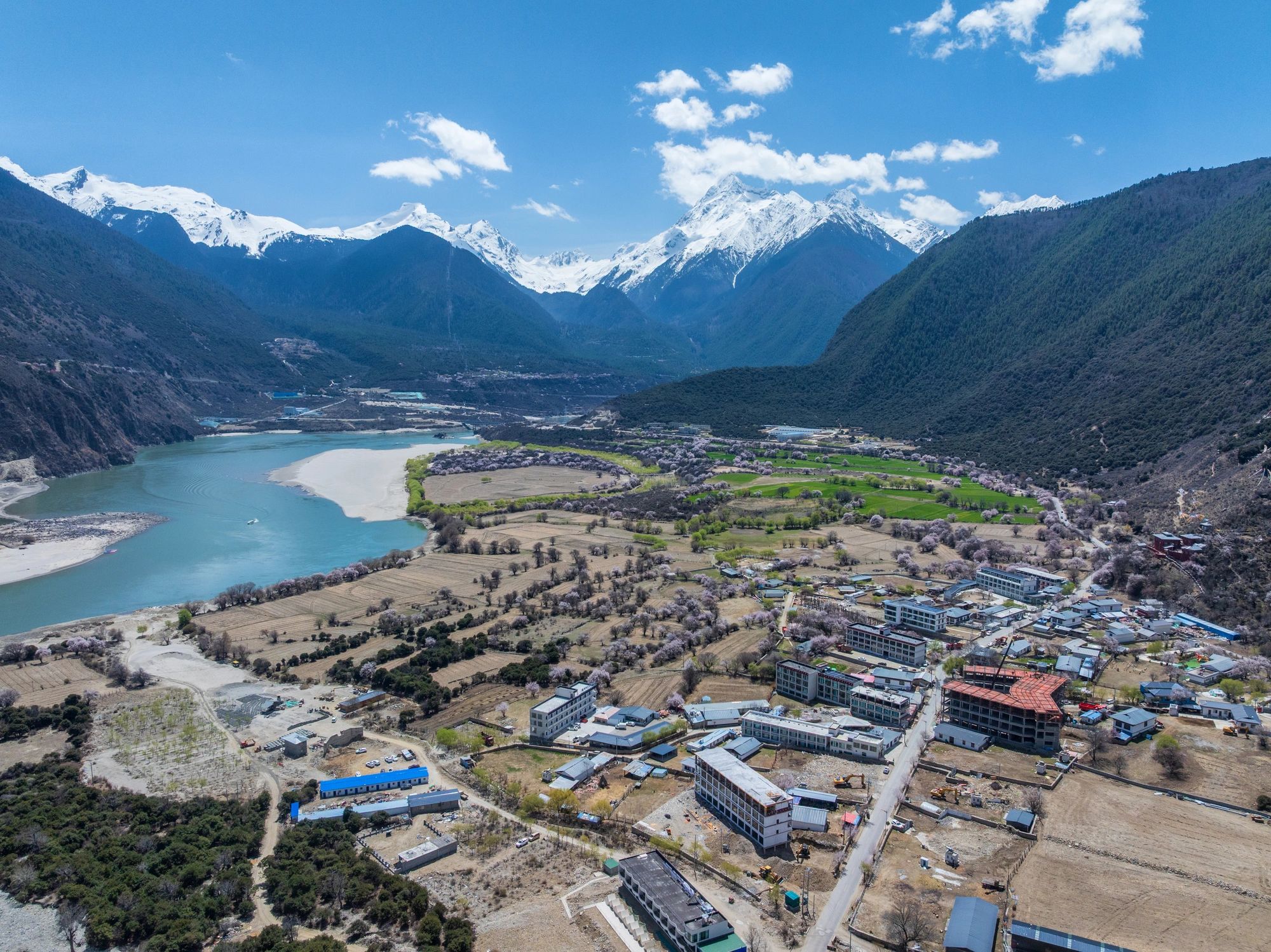 Aerial view of a valley surrounded by snow-capped mountains, featuring a river, fields, and scattered buildings, representing a popular region for trekking and expedition planning.