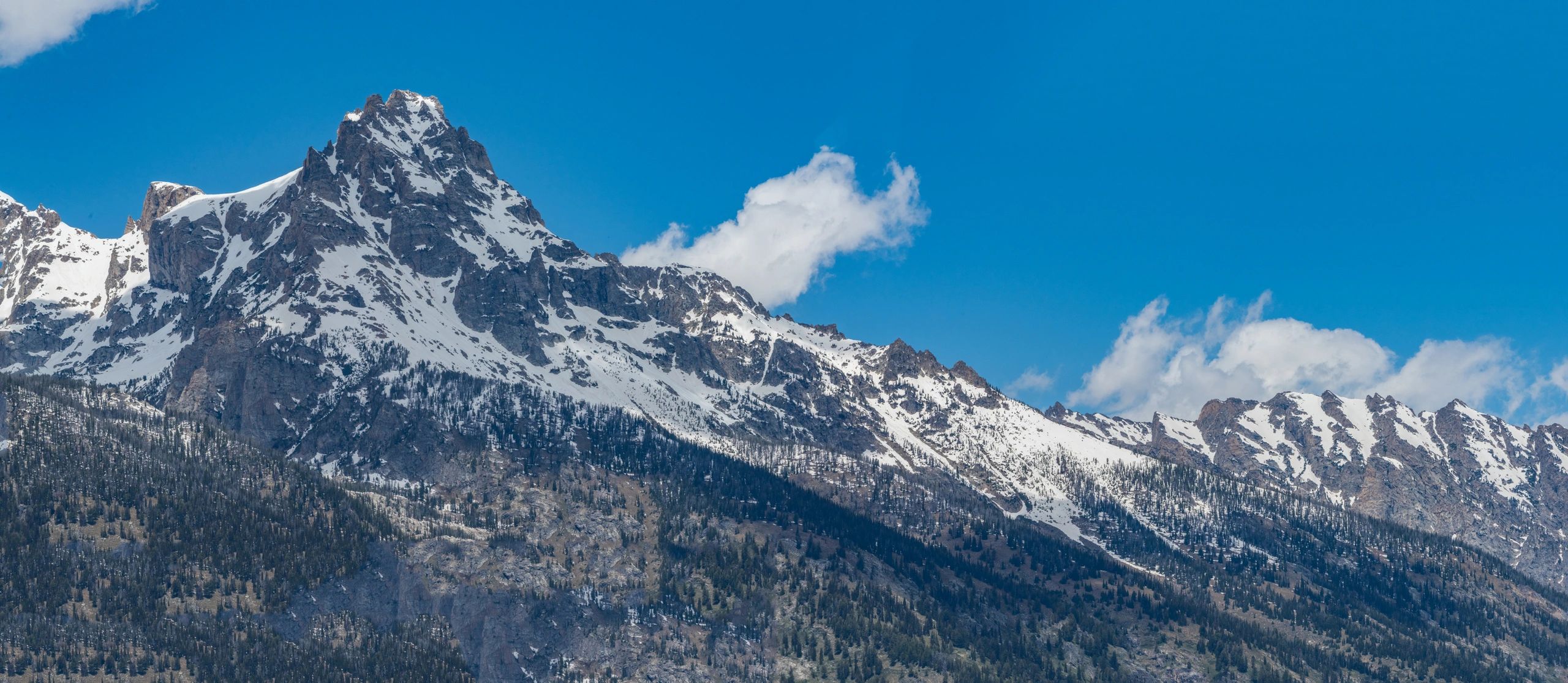 Snow-capped mountain range under a bright blue sky, showcasing rugged terrain and alpine scenery, relevant to climbing and hiking guides.