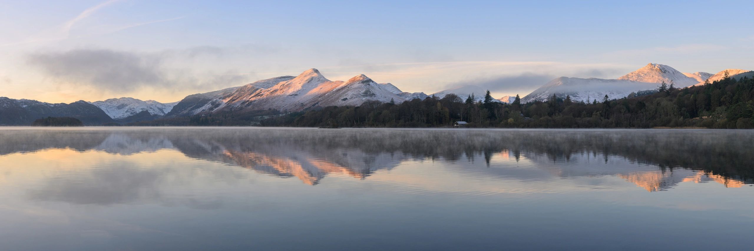 Mountain landscape reflecting in calm water at sunrise, showcasing snow-capped peaks and mist over the lake, emphasizing outdoor adventure and natural beauty for hikers and climbers.