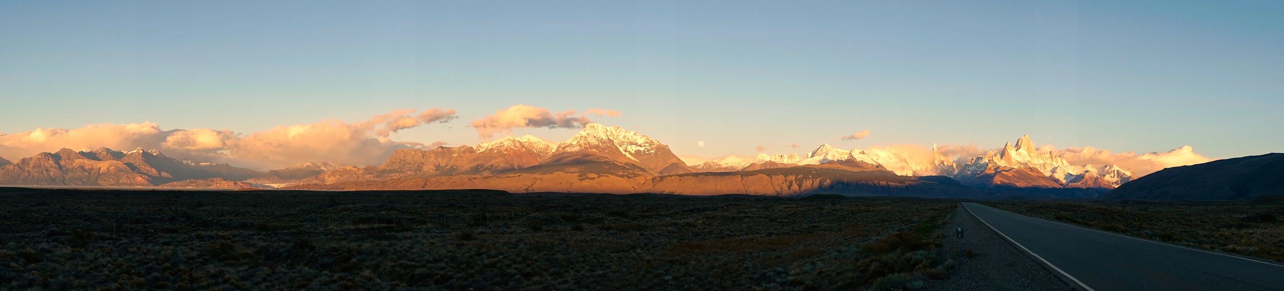 Panoramic view of majestic mountain range at sunset, showcasing snow-capped peaks and dramatic clouds, emphasizing the beauty of outdoor adventures and peak exploration.