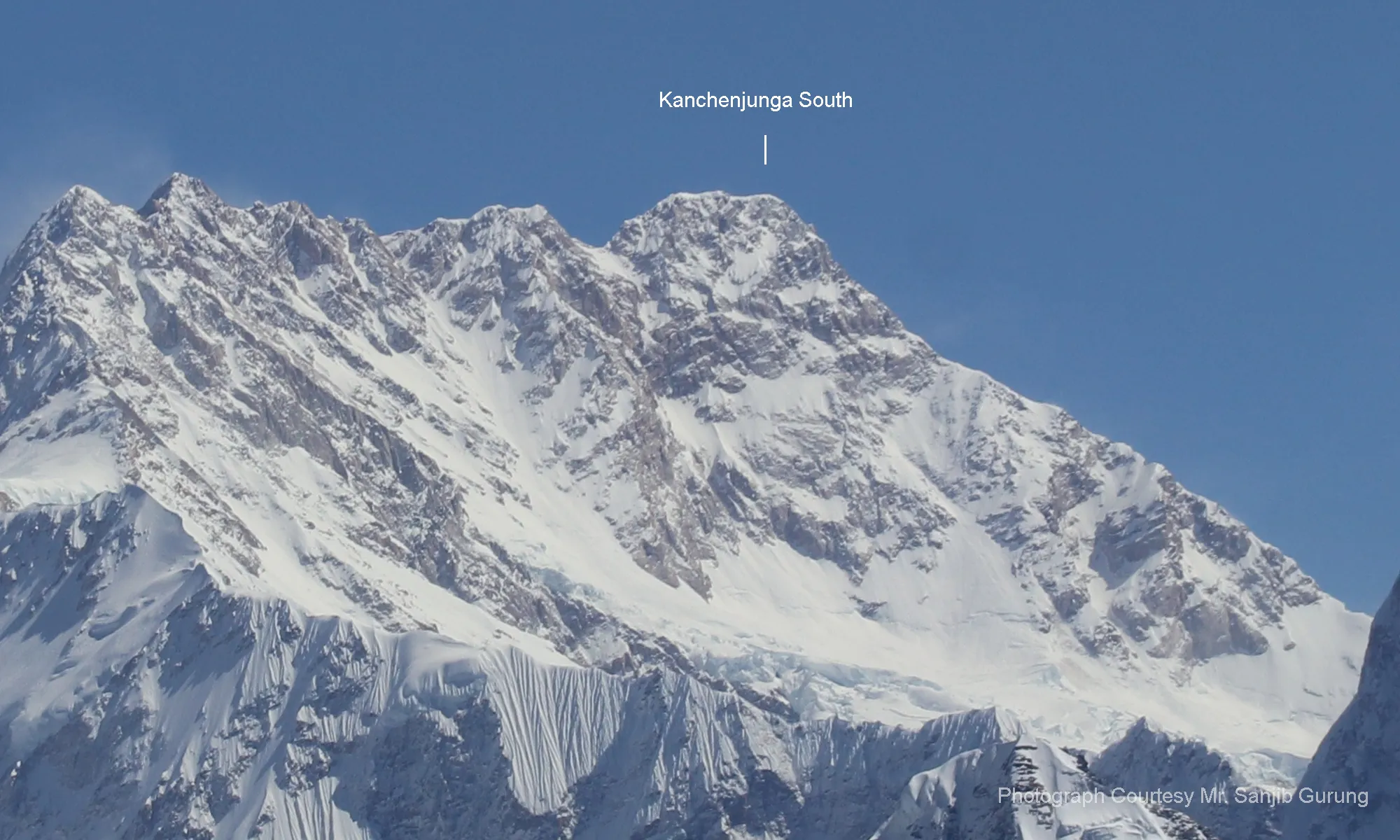 Kanchenjunga South peak against a clear blue sky, showcasing snow-covered slopes and rugged terrain, relevant to high-altitude mountaineering and climbing expeditions.