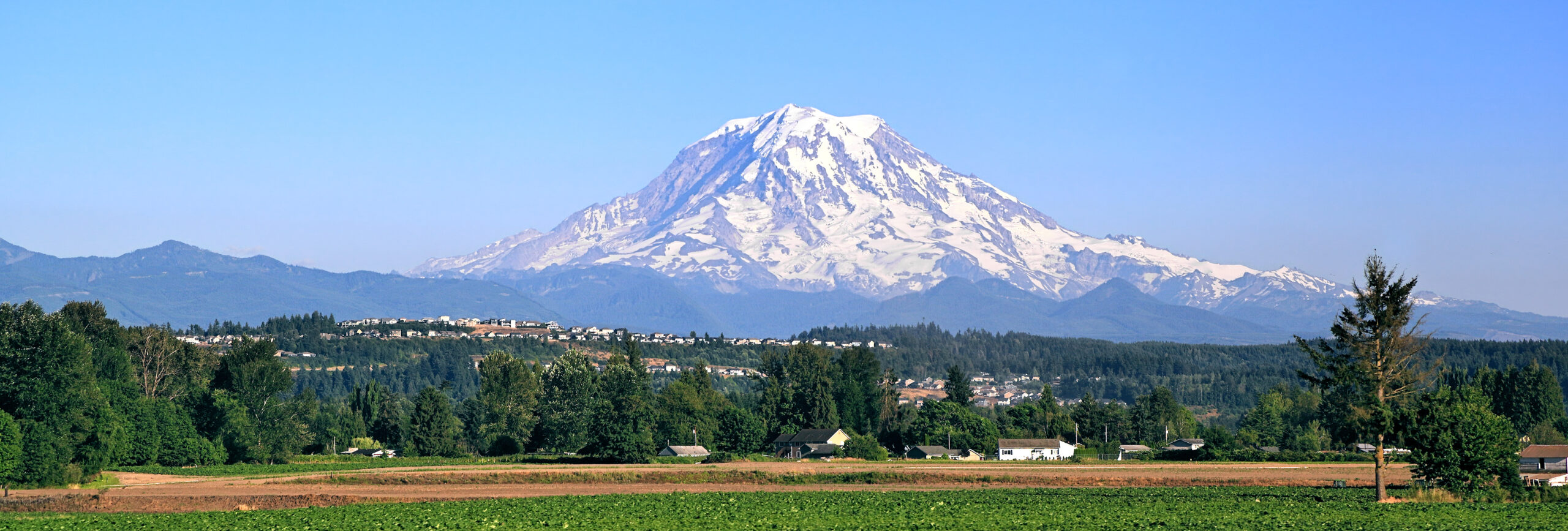 Mount Rainier at 14410 feet in the Cascade Range of Washington State USA showing the heavily glaciated stratovolcano towering over Pacific Northwest forest landscape — the highest volcanic peak in the contiguous United States and the most heavily glaciated mountain in the lower 48, first climbed 17 August 1870 by Hazard Stevens and Philemon Beecher Van Trump