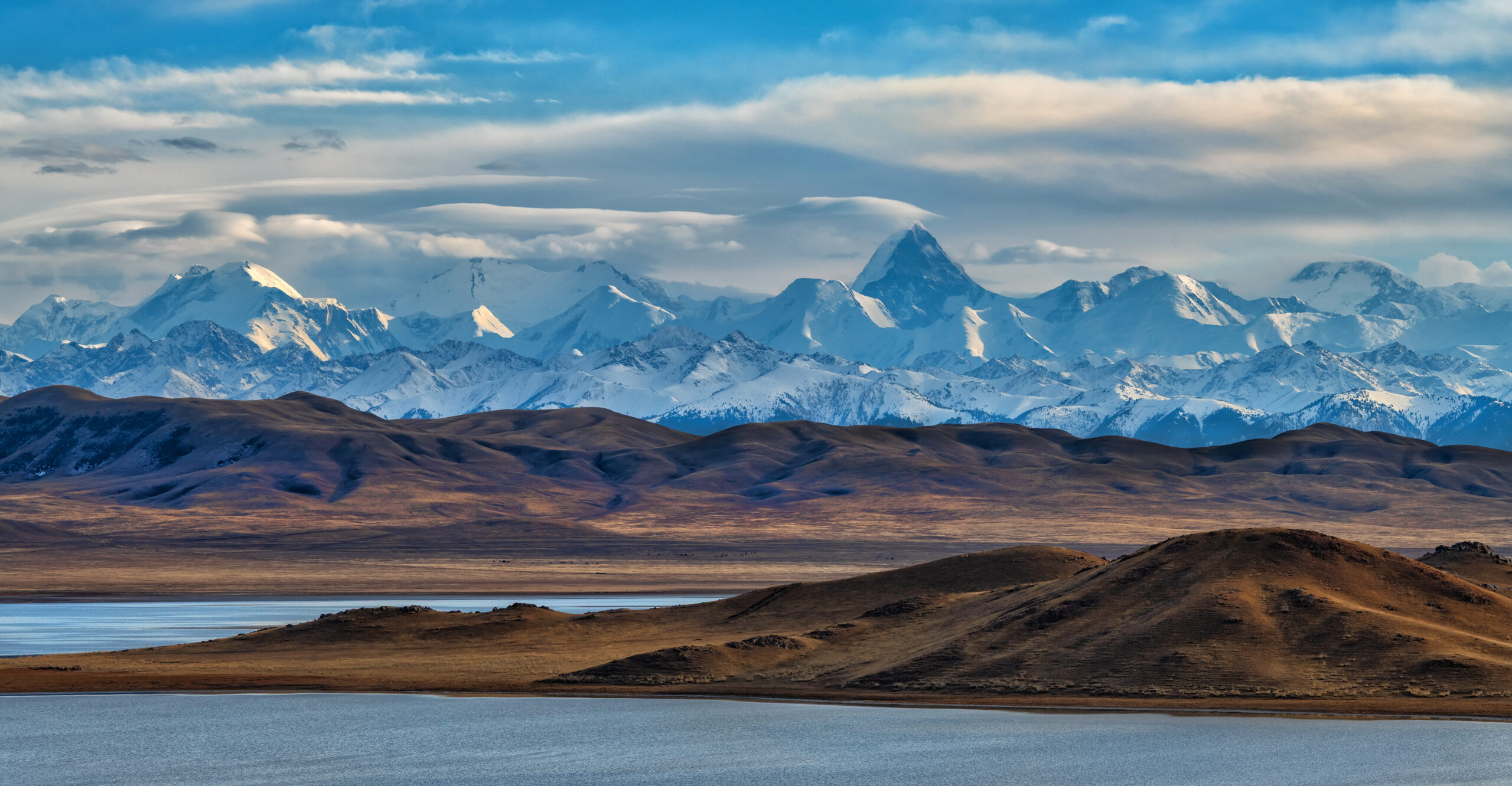 Khan Tengri at 7010 meters showing the iconic marble pyramid profile rising from the Central Tien Shan with the pink limestone summit glowing in alpenglow on the Kyrgyzstan Kazakhstan border during 2026 climbing season
