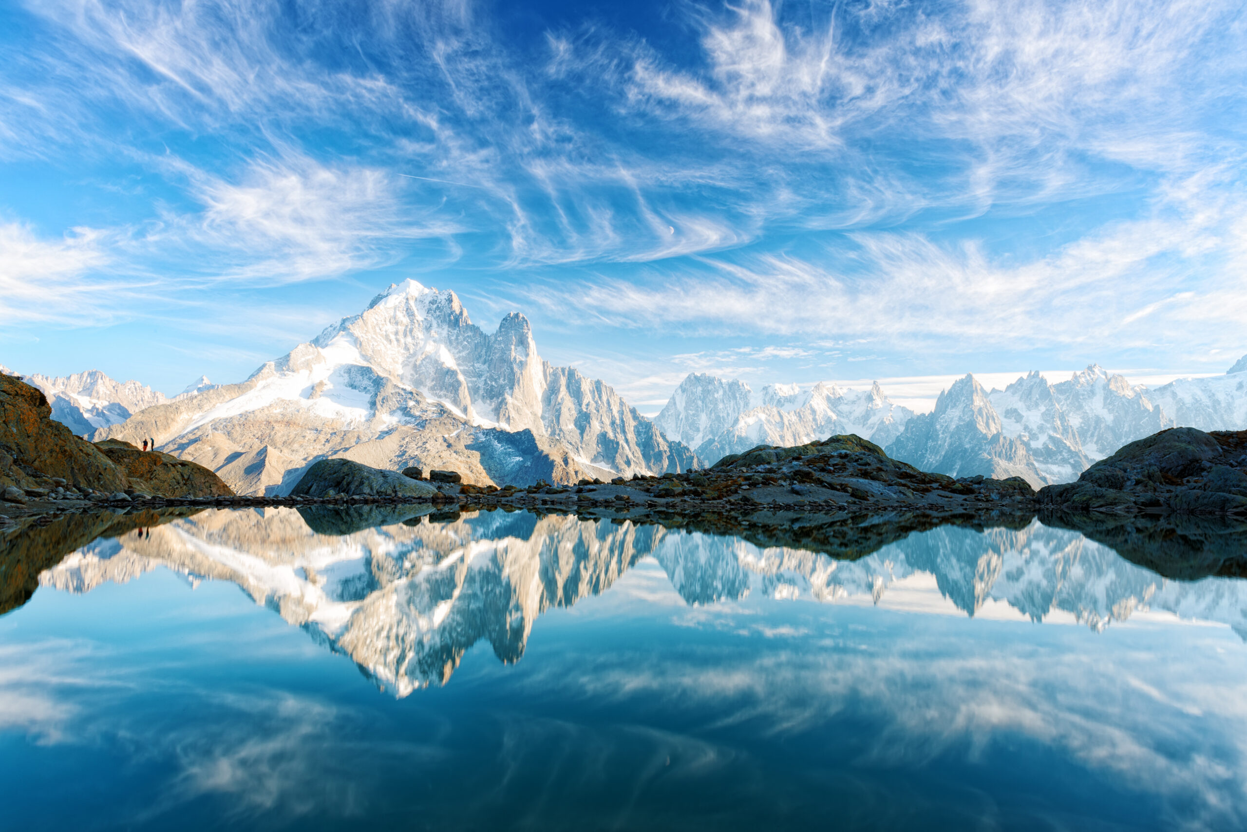 Scenic view of Mont Blanc reflecting in a tranquil lake, with rocky terrain and dramatic sky, relevant to the 2026 expedition via the Goûter Route.