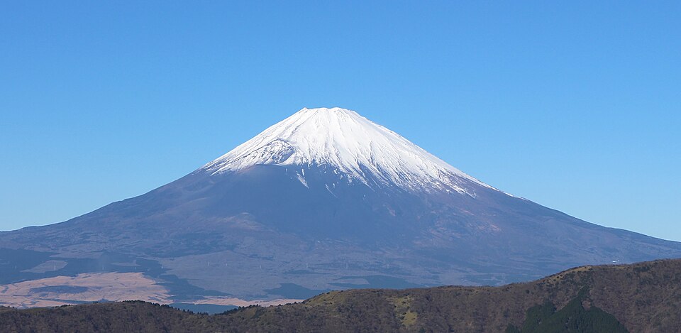 Mount Fuji with snow-capped peak against a clear blue sky, representing a prominent climbing destination in Japan.