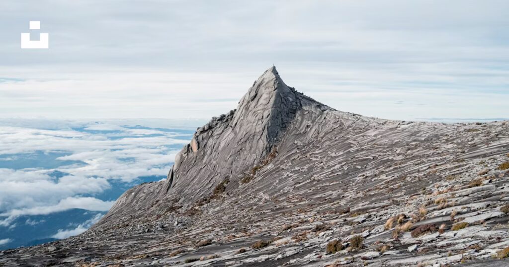 Mount Kinabalu summit peak with rugged granite terrain and cloudy sky, illustrating climbing challenges and weather conditions for ascents.