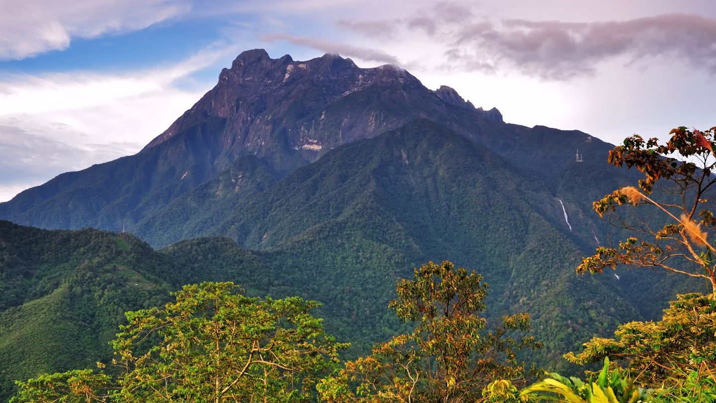 Mount Kinabalu towering over lush green forests, showcasing its rugged summit and dramatic landscape, a prominent feature in the Malaysian climbing guide.