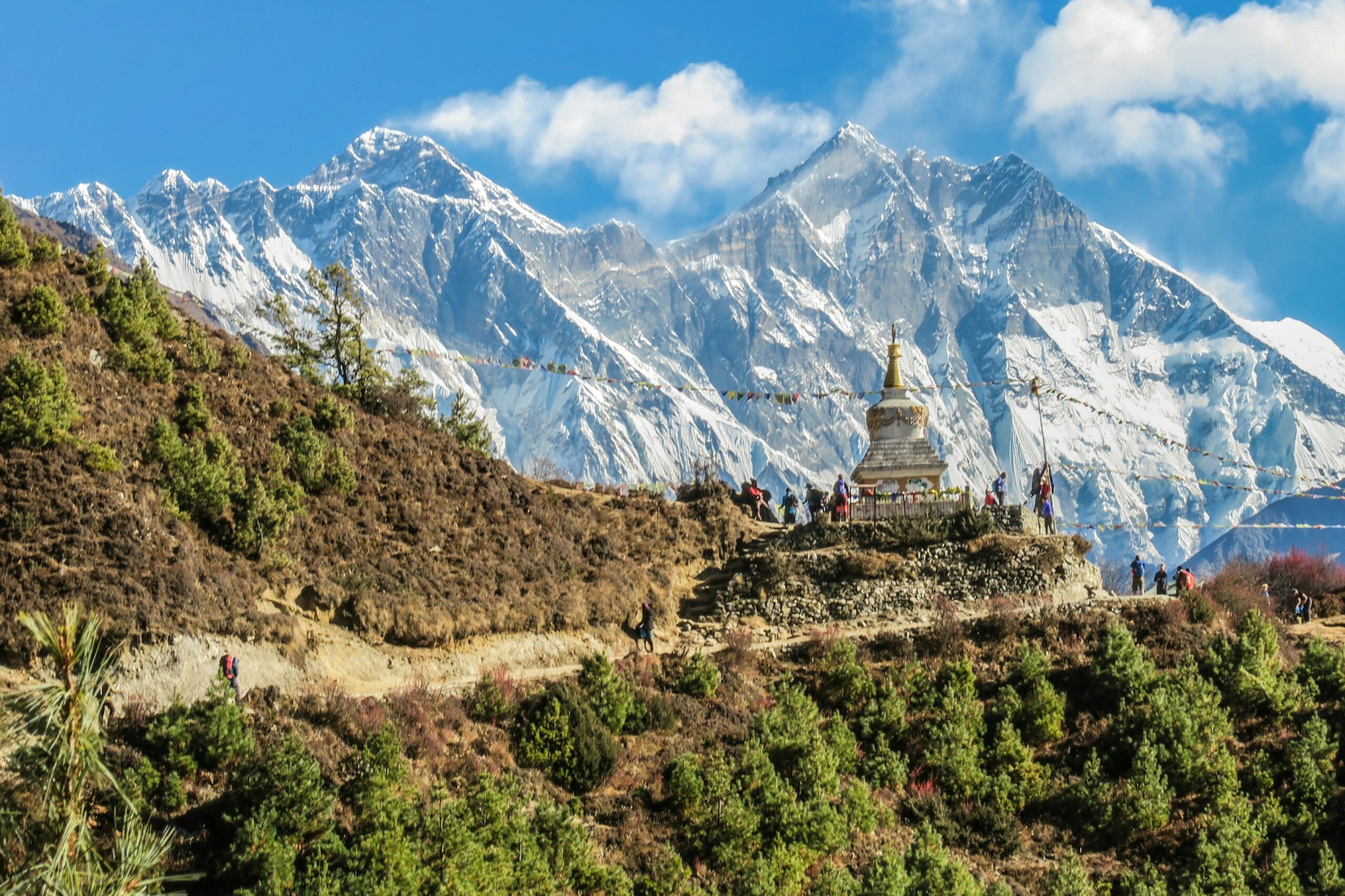 Scenic view of Mount Everest region featuring snow-capped peaks, a traditional stupa, and trekkers along a hiking path, emphasizing preparation for high-altitude climbing.