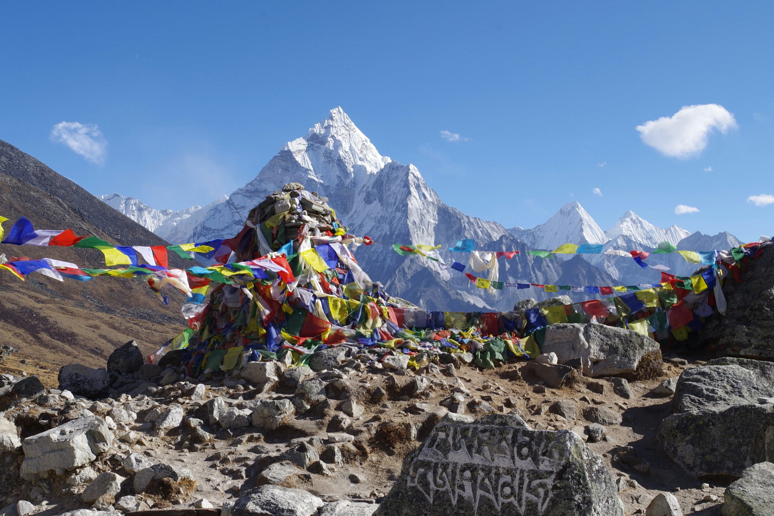 Prayer flags and stone cairn in foreground with snow-capped Ama Dablam mountain in background, symbolizing alpine climbing and cultural significance in Nepal.