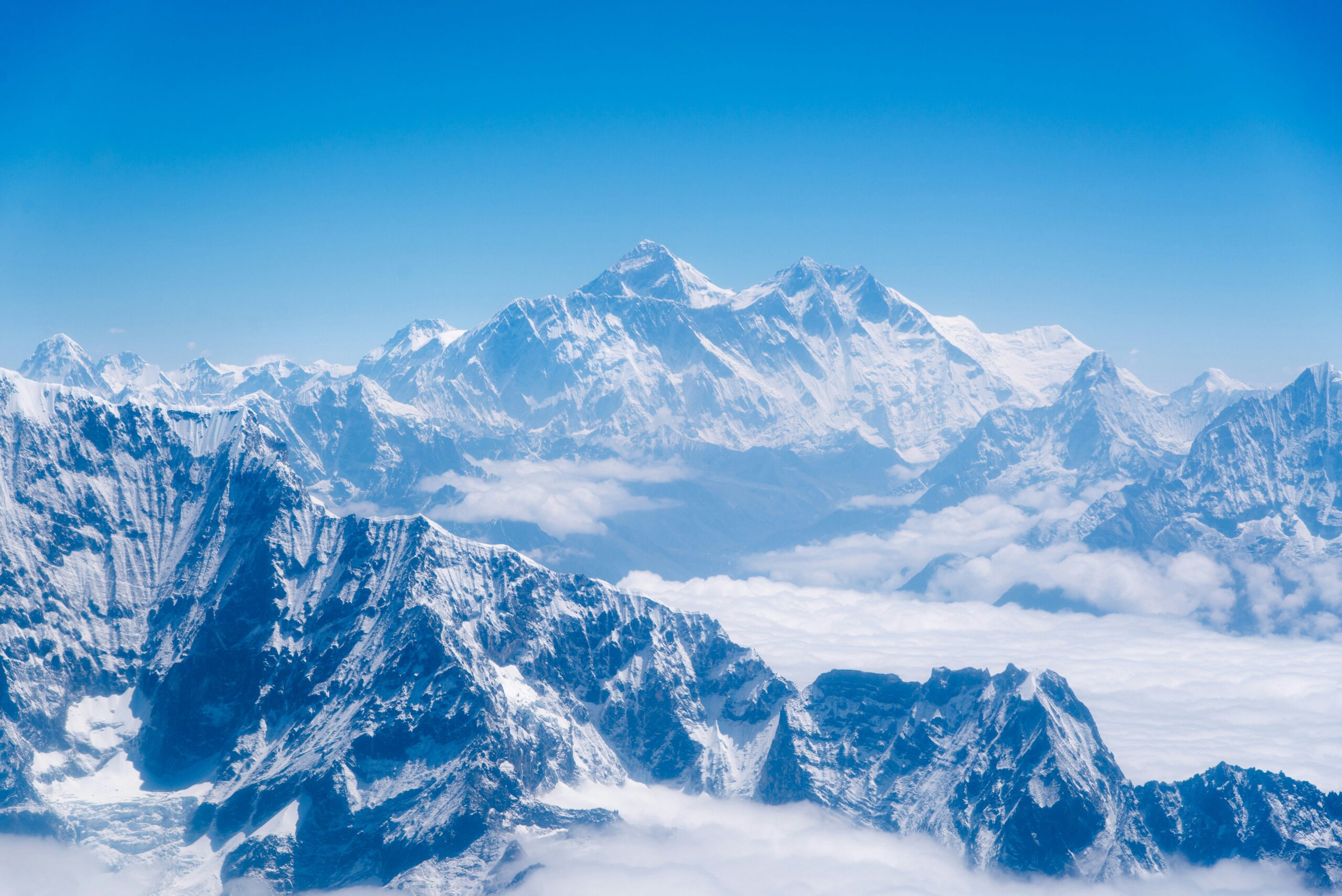 Snow-capped peaks of Mount Everest and surrounding Himalayas under a clear blue sky, illustrating the majestic landscape crucial for climbers considering weather conditions for expeditions.