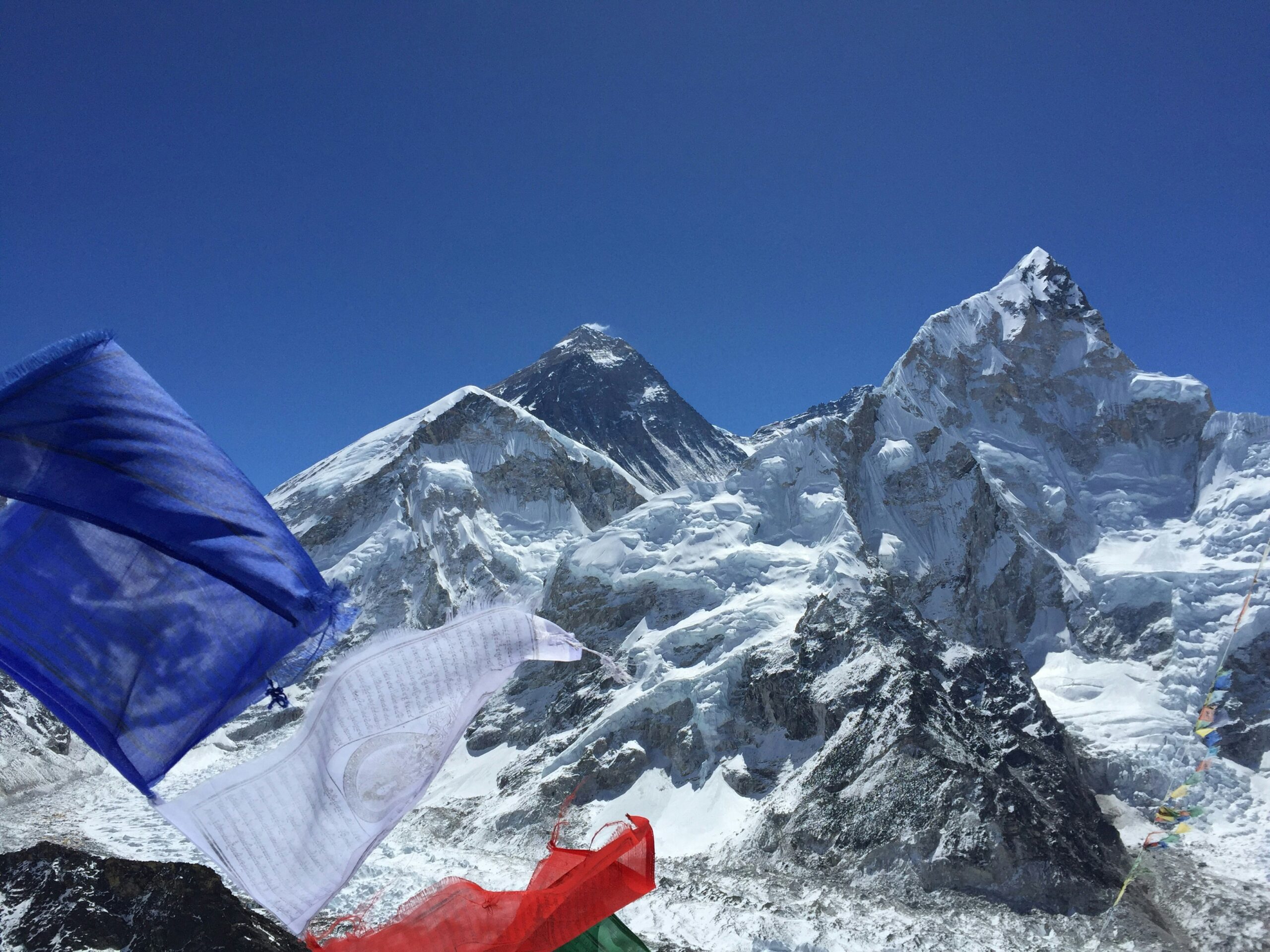Snow-capped peaks of Mount Everest and surrounding mountains, with colorful prayer flags in the foreground, symbolizing the spiritual journey of climbers on the South Col Route.