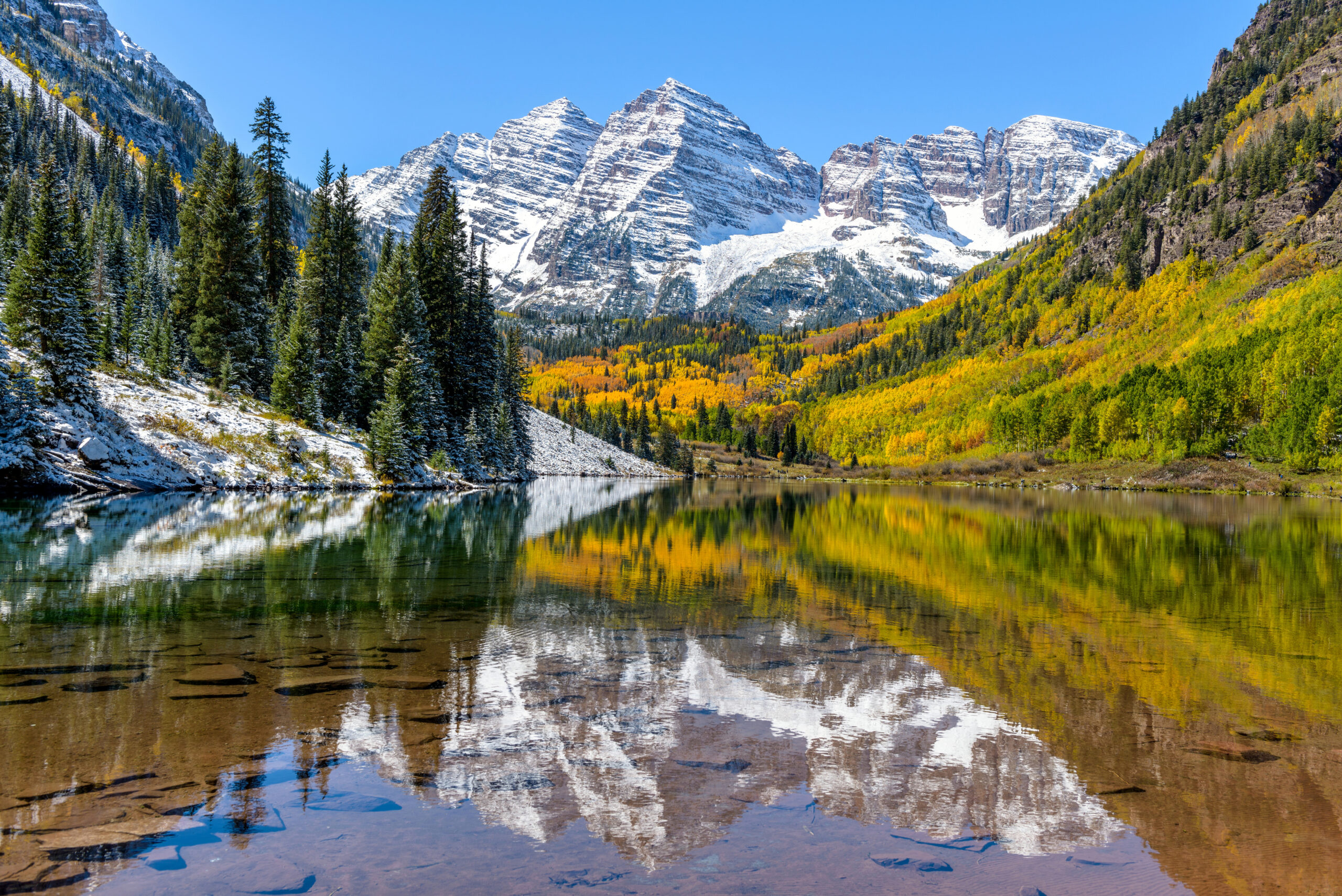 Maroon Peak and the Maroon Bells at 14163 feet in Colorado Elk Mountains showing the iconic pyramid profiles reflected in Maroon Lake during 2026 summer season the most photographed scene in Colorado