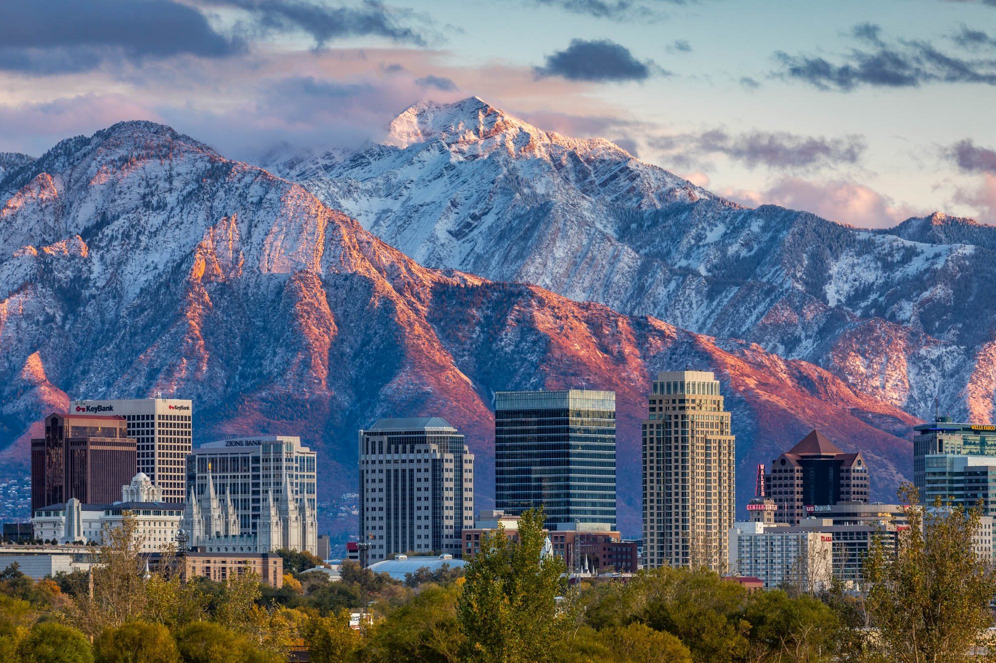 Salt Lake City skyline with snow-capped Wasatch Mountains in the background during sunset, highlighting outdoor adventure opportunities for hiking and climbing.