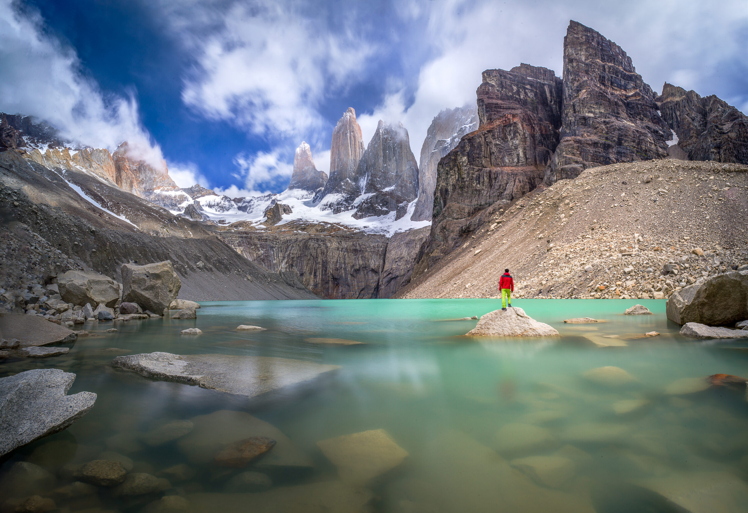 Hiker in an insulated red jacket facing dramatic mountain peaks