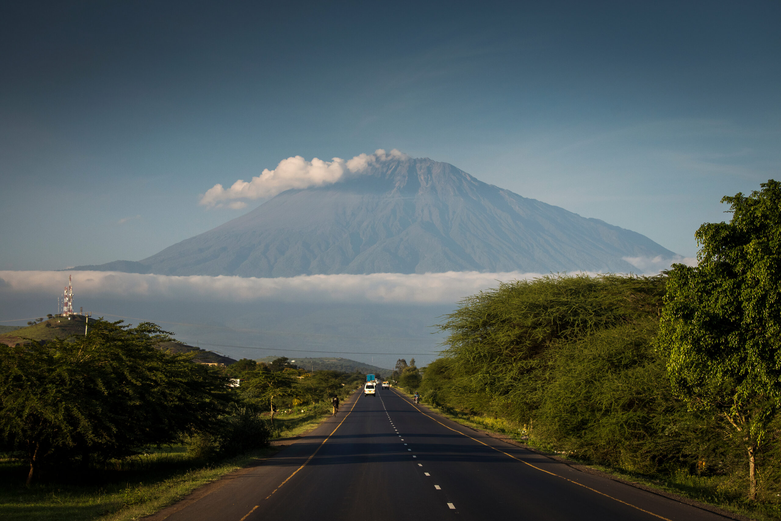 Mount Meru summit shrouded in clouds above a road and savanna landscape