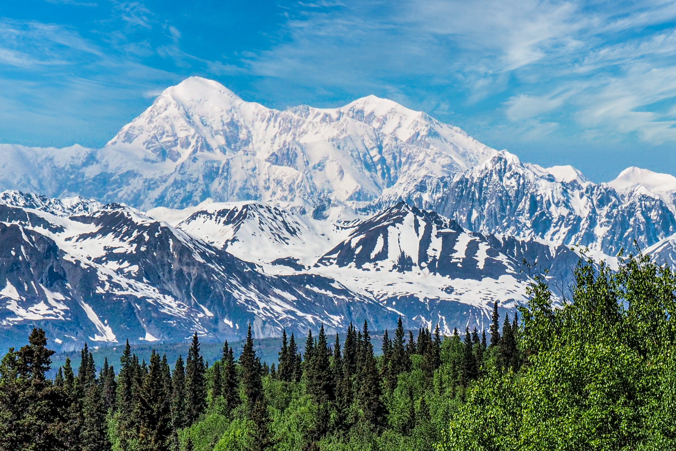 Climbers moving across a glacier below Denali under a clear sky