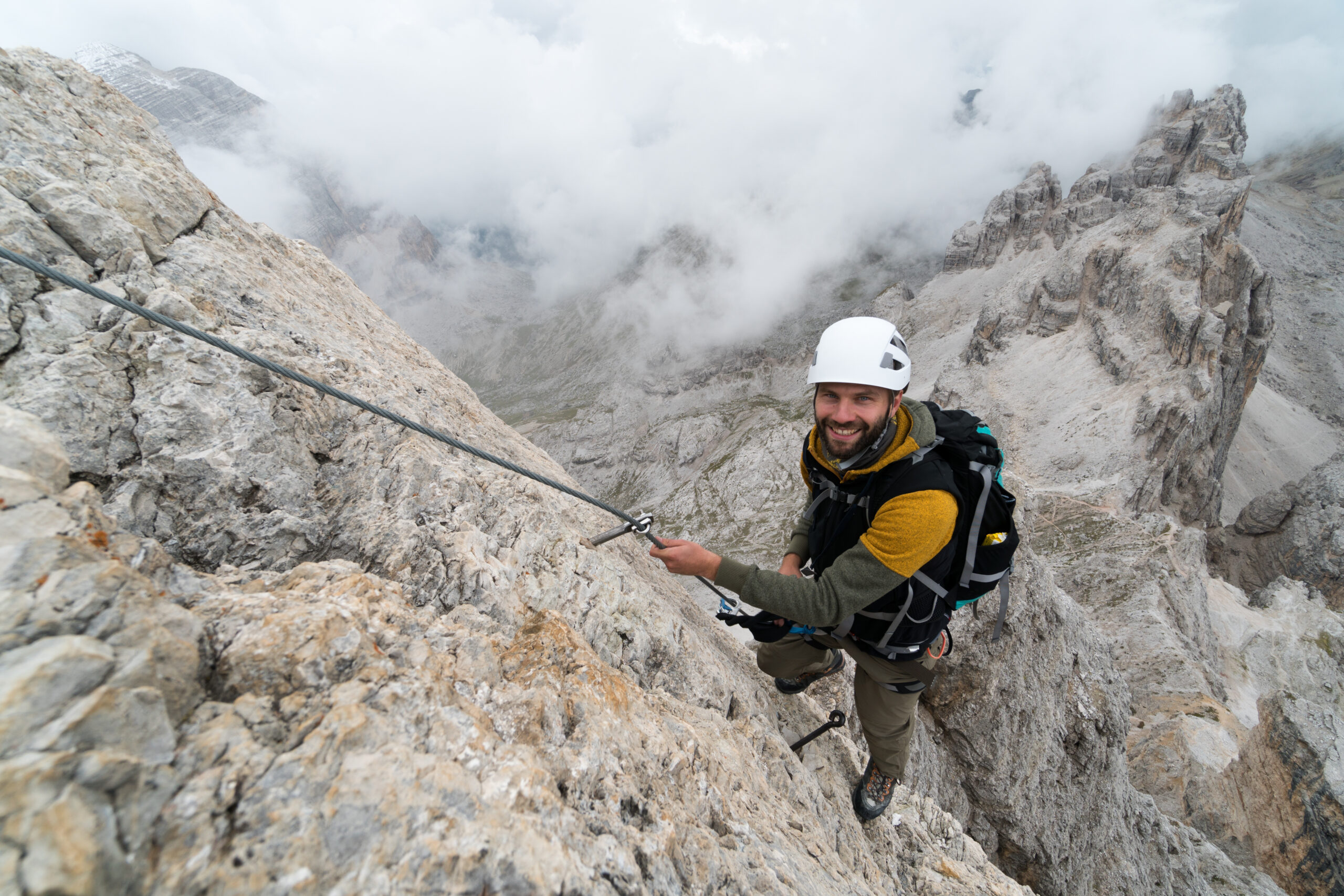 A climber descending a steep rock face on rappel using a belay device and harness