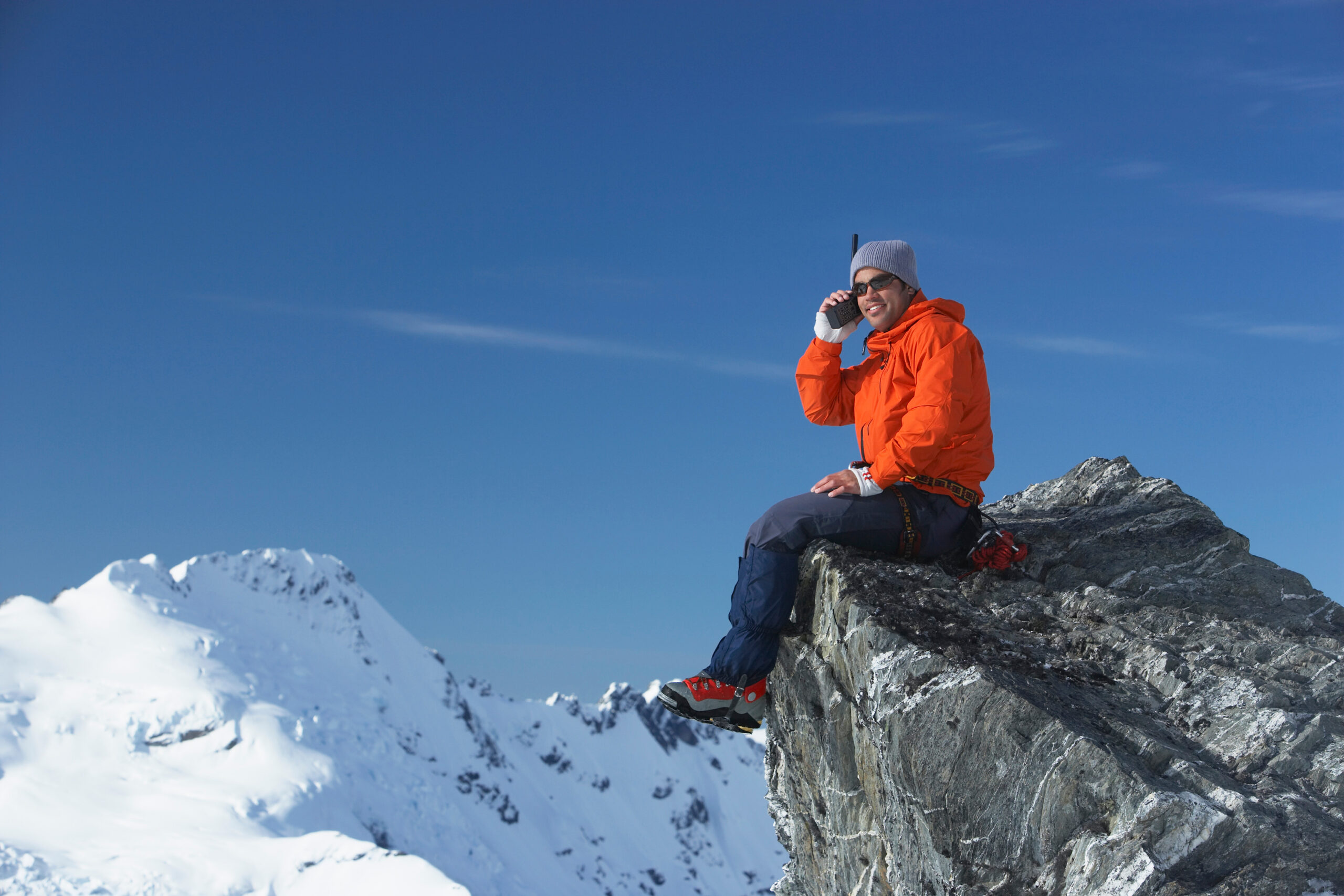 A hiker using a handheld satellite communicator device on a remote mountain ridge
