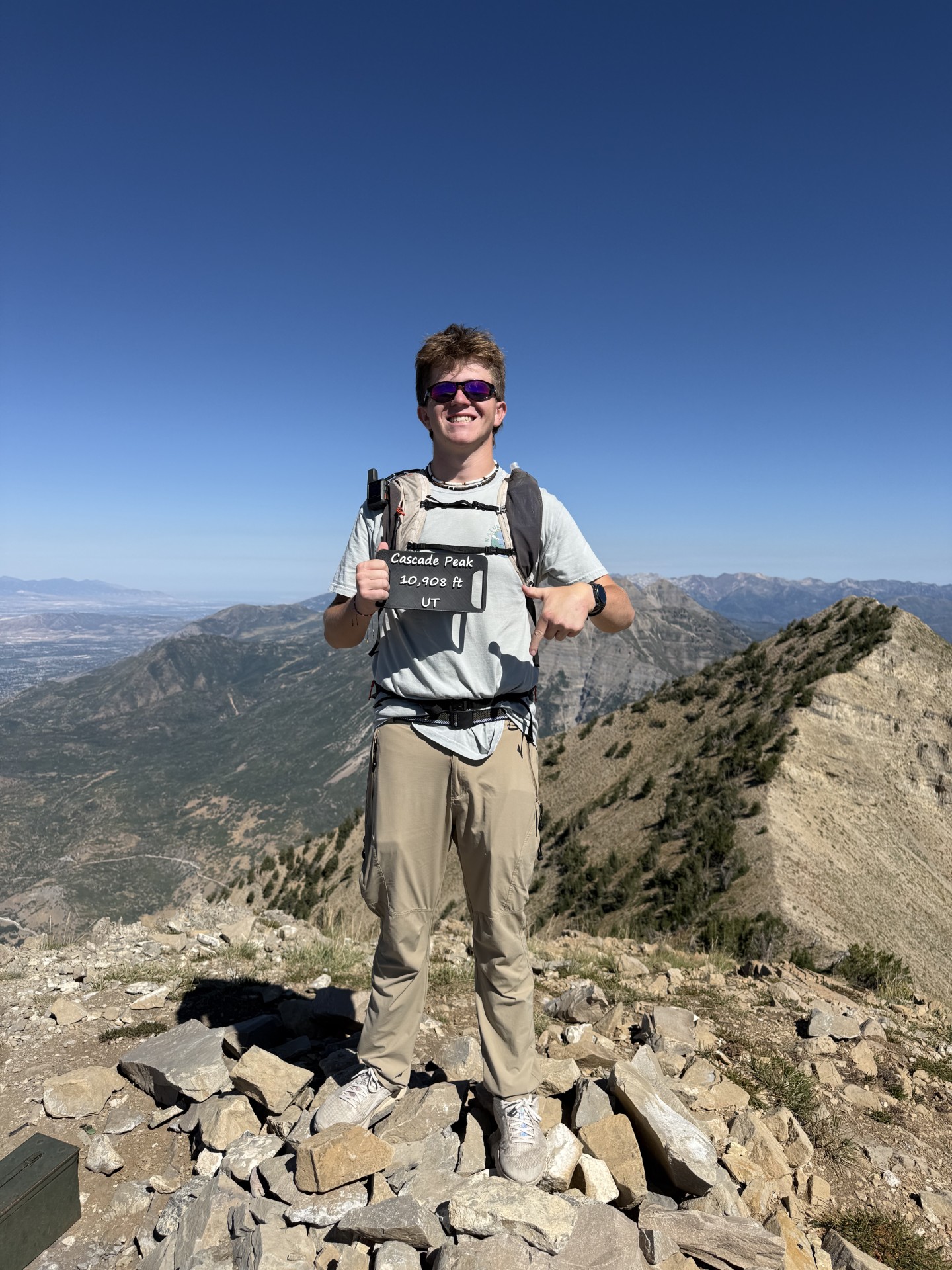 Climber holding a Cascade Peak 10,908 foot summit sign above Utah Valley