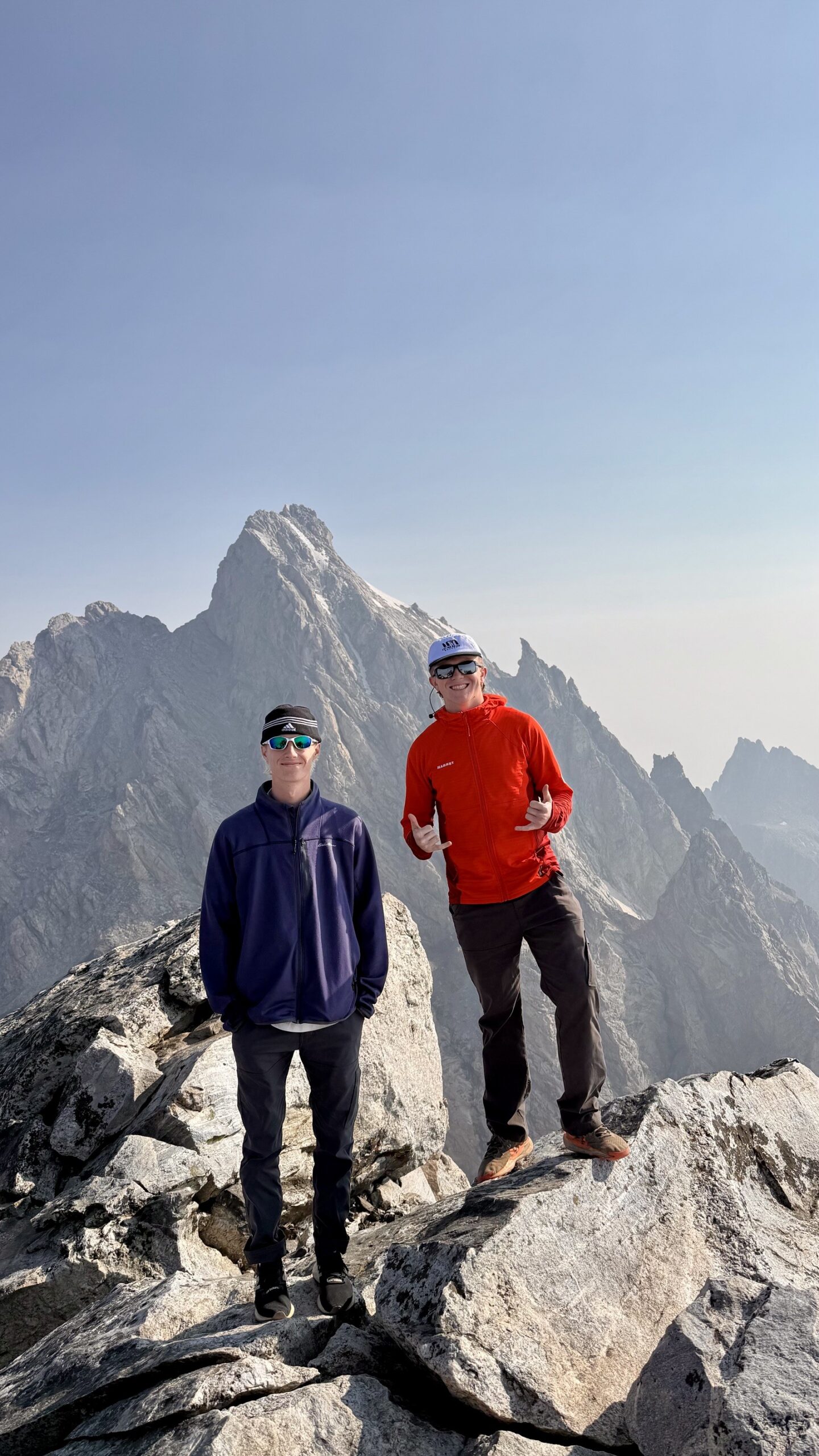 Dawson and a climbing partner standing on high Teton rock with a jagged summit behind them